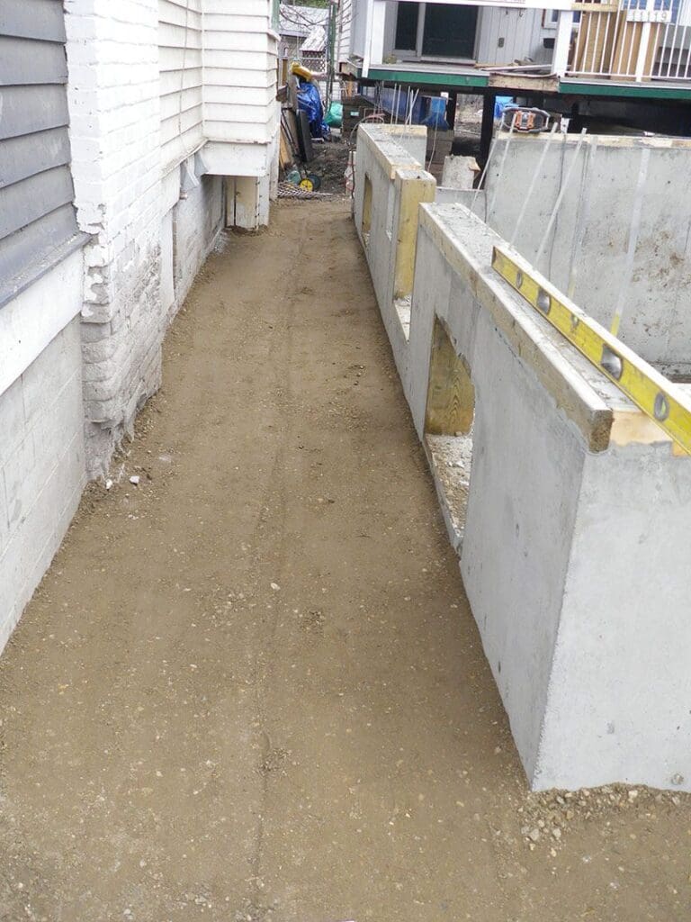 Professional contractor examines foundation underpinning costs and repair methods at residential construction site.